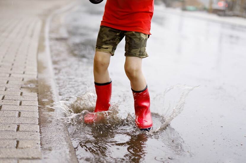 Kind met rode regenlaarzen in plas water